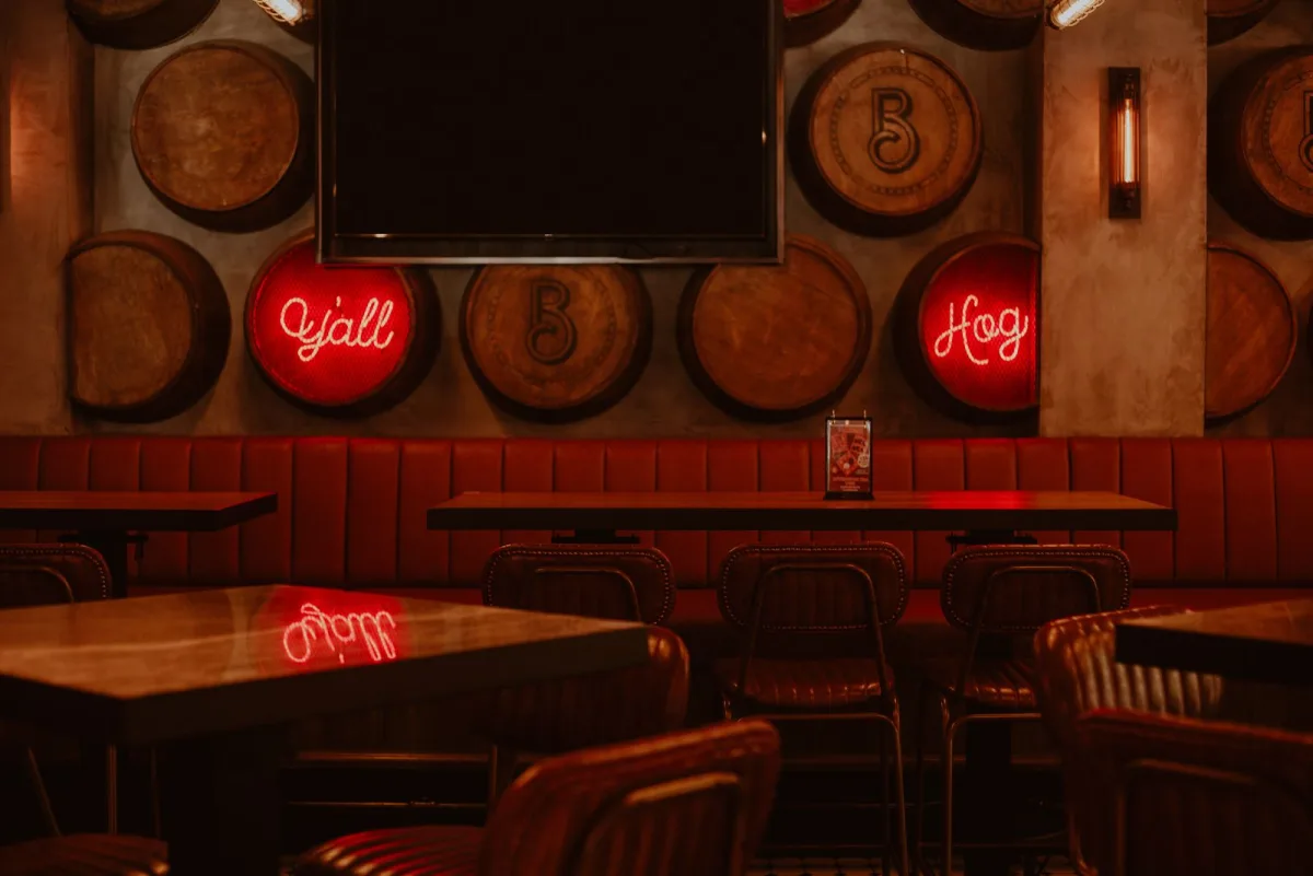 A bar where red neon signs, red leather booths, and warm wood barrels all share one bold, high-contrast palette