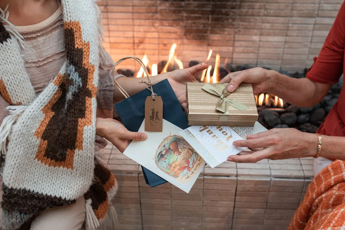 Two people exchanging wrapped gifts and cards in front of a fire