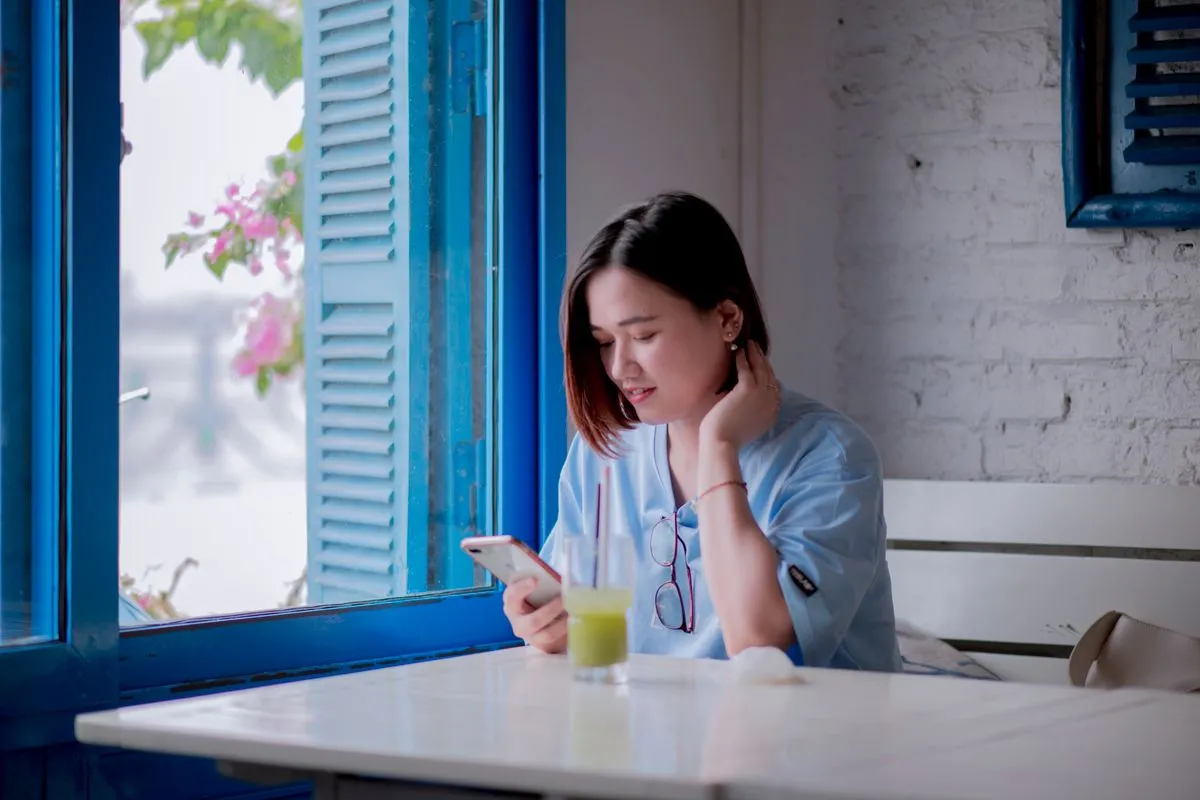 A guest sitting alone at a cafe table by a window, looking at her phone